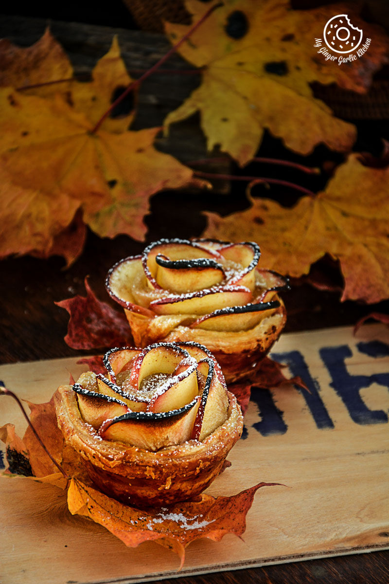two apple rose mini tartlets on a wooden board with leaves