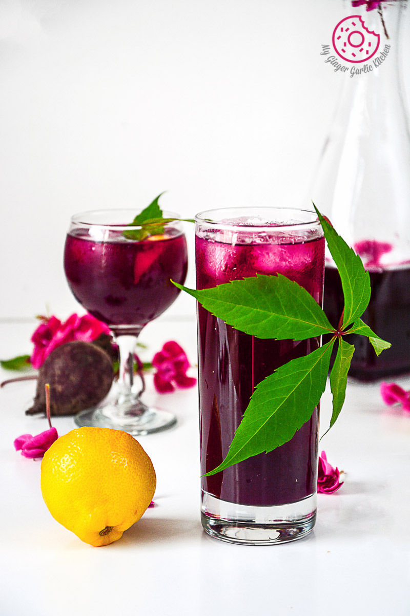 two glasses of beet lemonade with a pitcher and a pink flowers