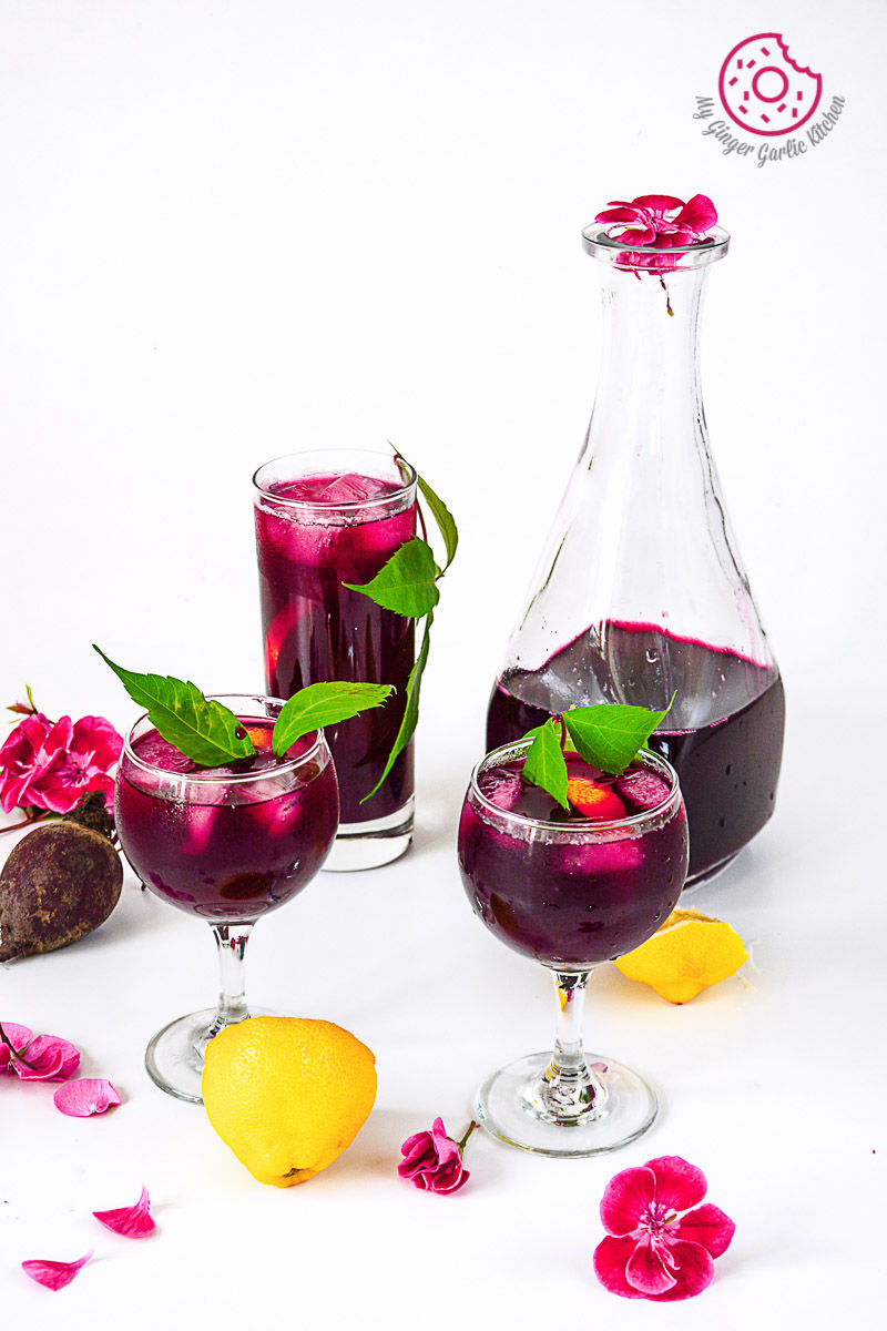 three glasses of beet lemonade and a pitcher, lemons and flowers