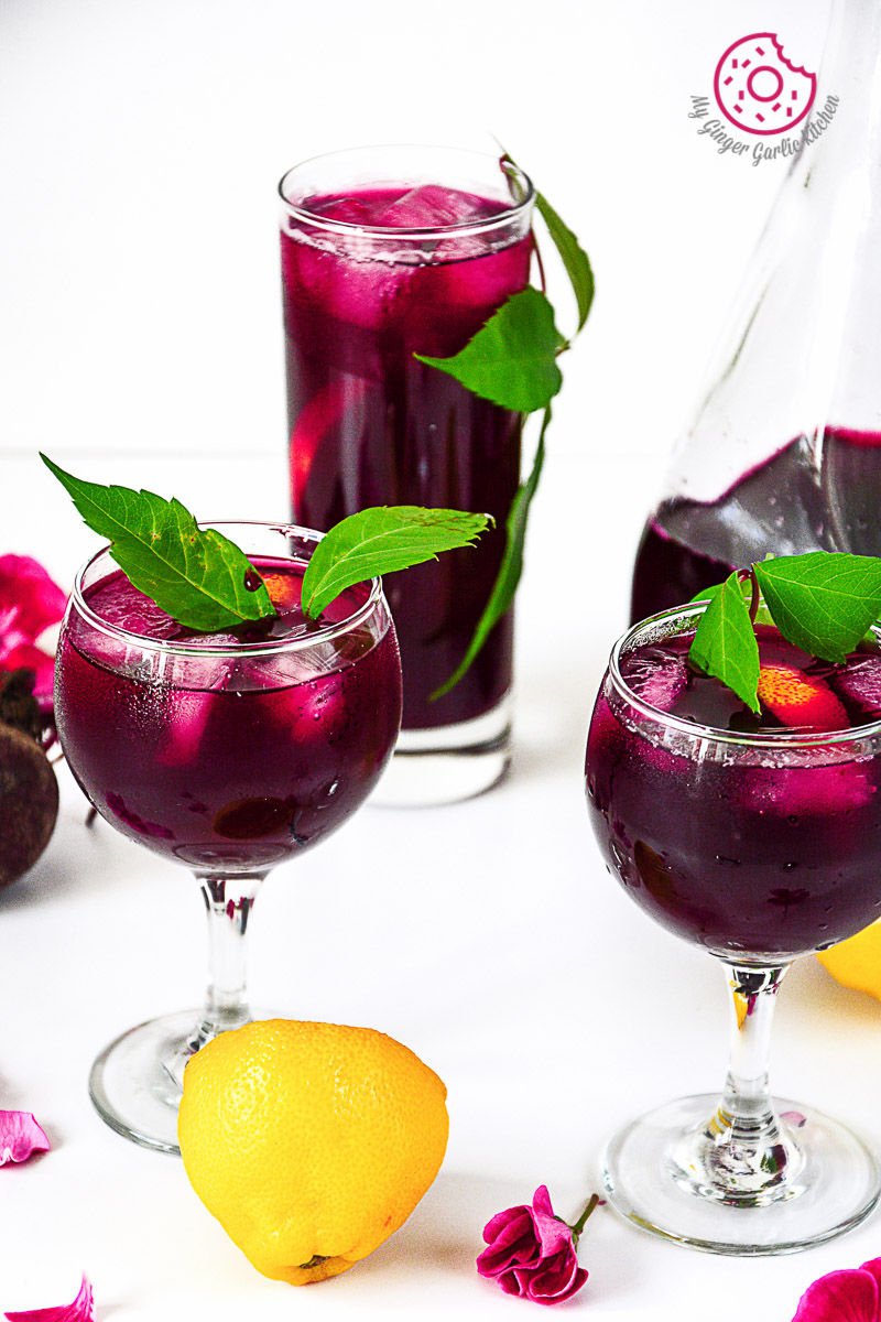 three glasses of beet lemonade with fruit and a pitcher