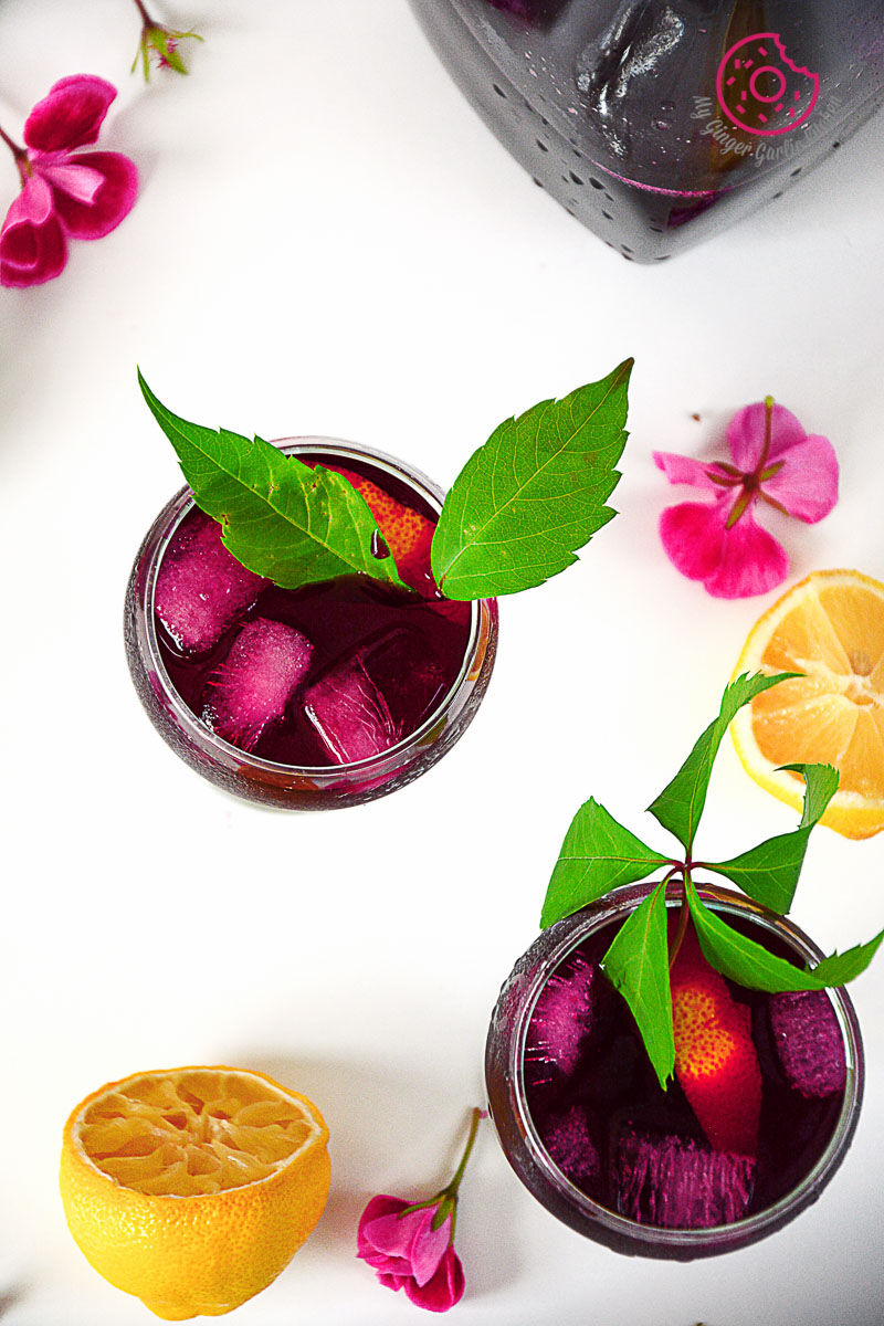 two glasses of beet lemonade and ice and flowers on a table