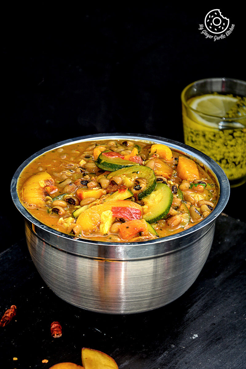 a bowl of black eyed bean zucchini peach curry that is sitting on a table with a glass of water