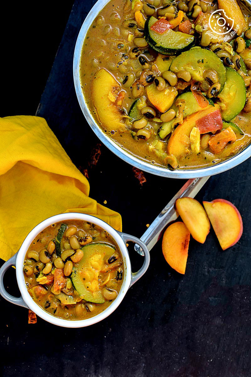 two bowls of black eyed bean zucchini peach curry with peach slices on a table