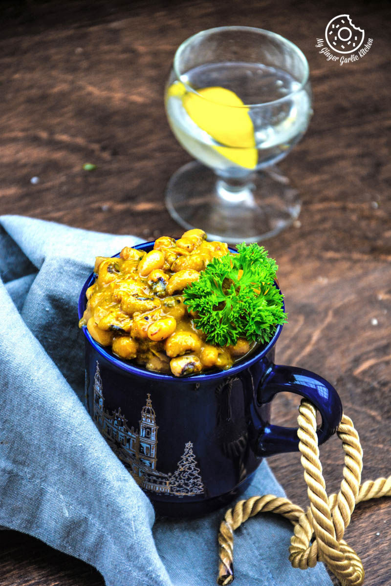 a blue cup filled with black eyed pea curry in pepper onion gravy on a table