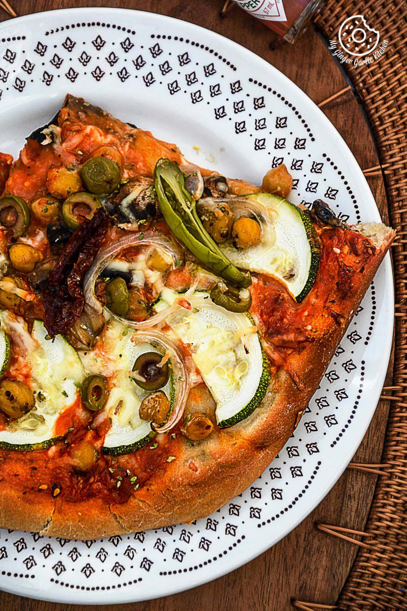 a slice of chickpea zucchini mushroom pizza with and olives on a plate on a table