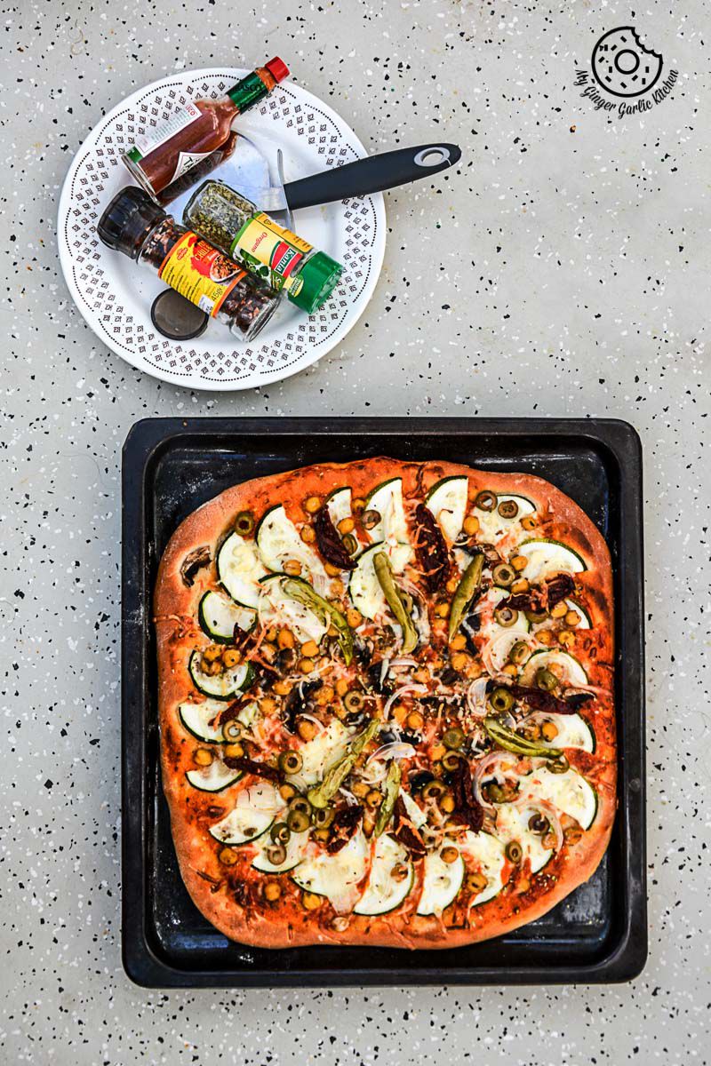 a chickpea zucchini mushroom pizza with and olives with a plate of vegetables