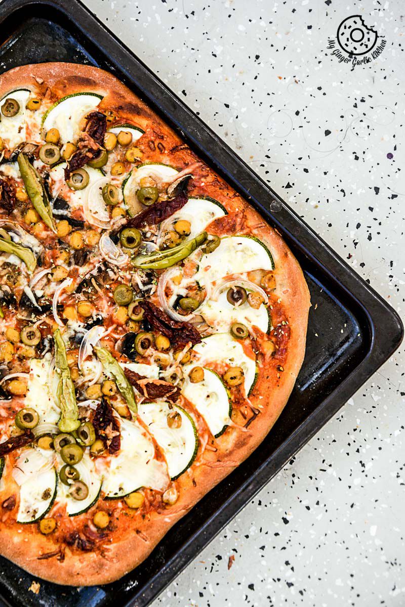 a chickpea zucchini mushroom pizza with and olives and other toppings on it on a pan