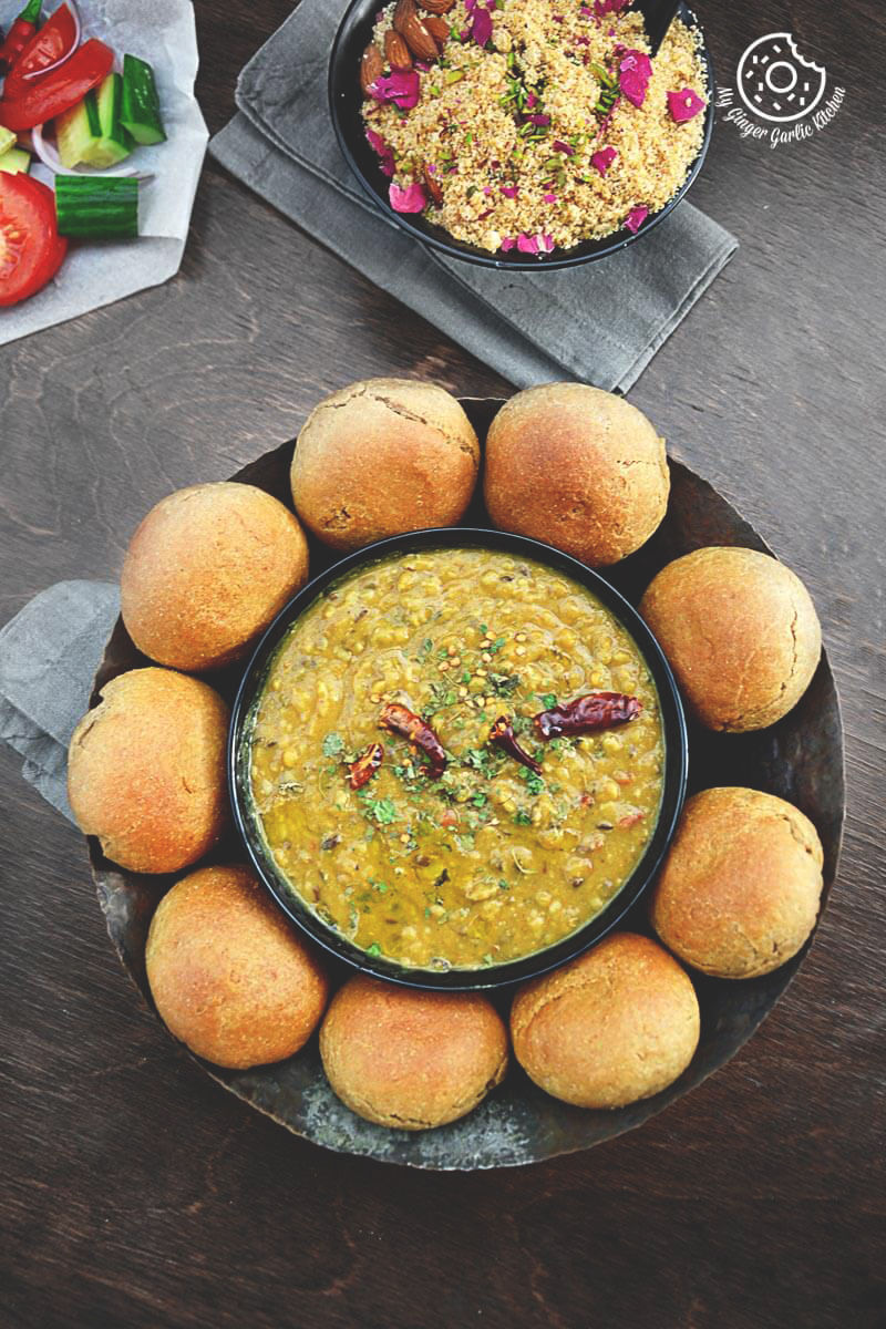 a bowl of dal and bati on a plate with some churma and salad on side