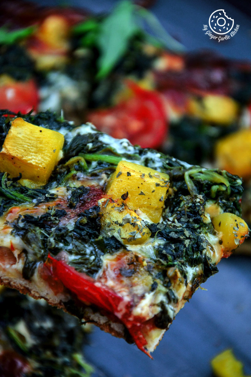 a slice of garlicky spinach mango tomato pizza being held up