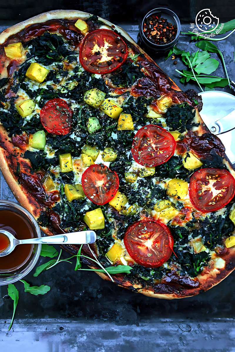 garlicky spinach mango tomato pizza in a tray on a table