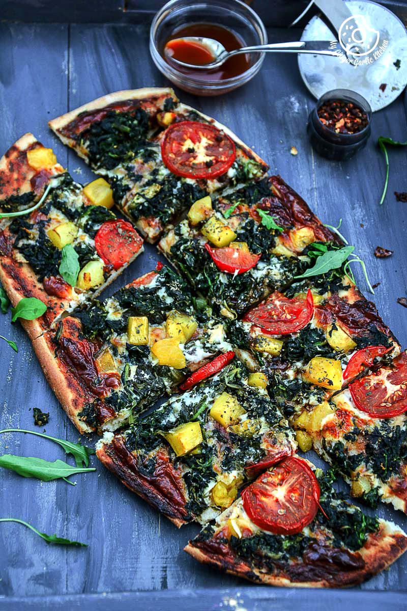 garlicky spinach mango tomato pizza with pepper flakes and pizza cutter on side