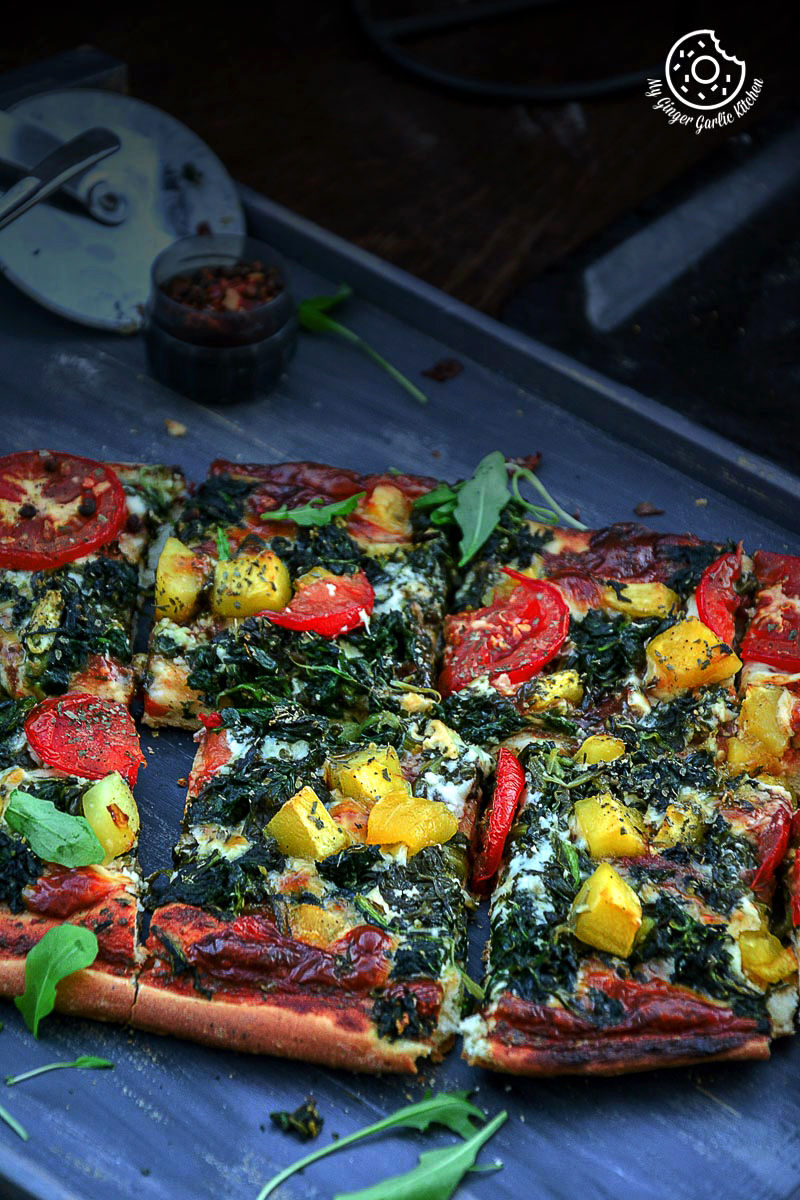 a garlicky spinach mango tomato pizza with many toppings on a tray