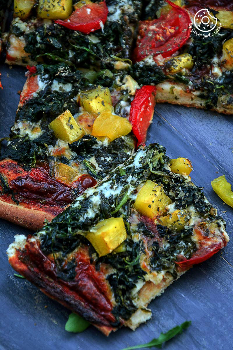 garlicky spinach mango tomato pizza and other toppings on a blue plate