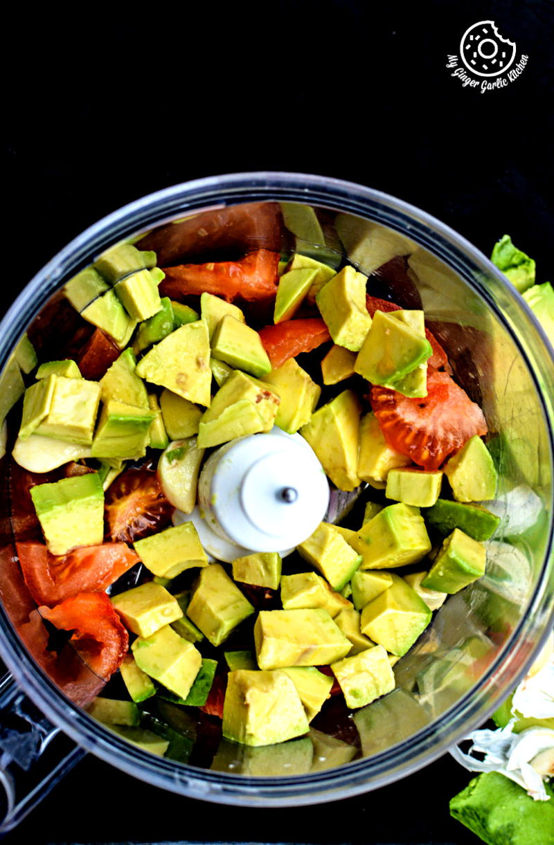 a food processor with avocado and tomatoes in it