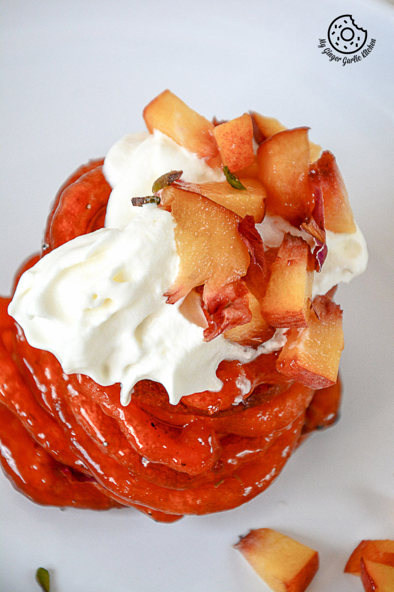 a plate with a instant peach jalebi with whipped cream and chopped peaches