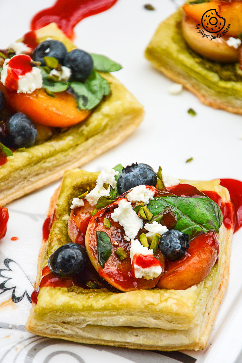 four square peach pesto tart with blueberries and basils with fruit and cheese on them
