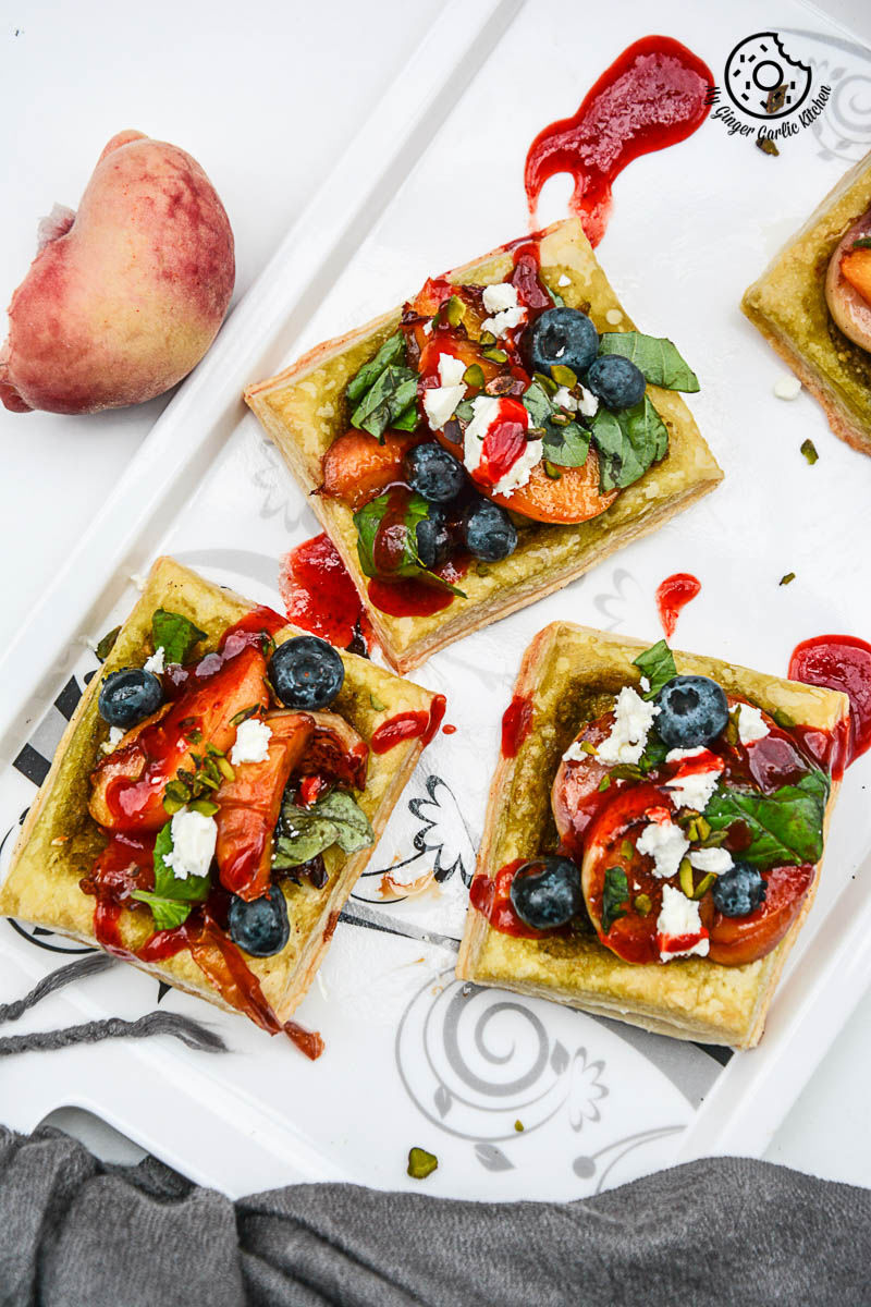 four square peach pesto tart with blueberries and basils with fruit and cheese on a tray