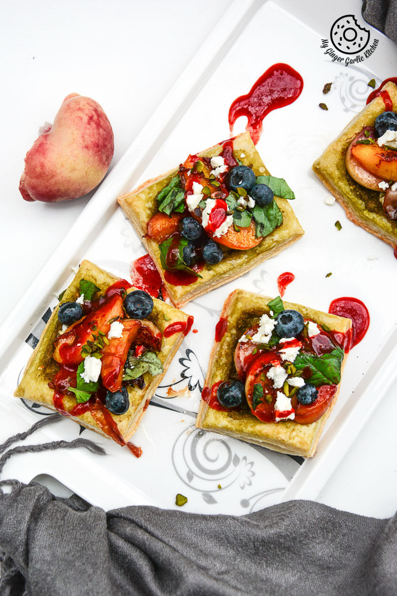 four square peach pesto tart with blueberries and basils with fruit and cheese on a white plate