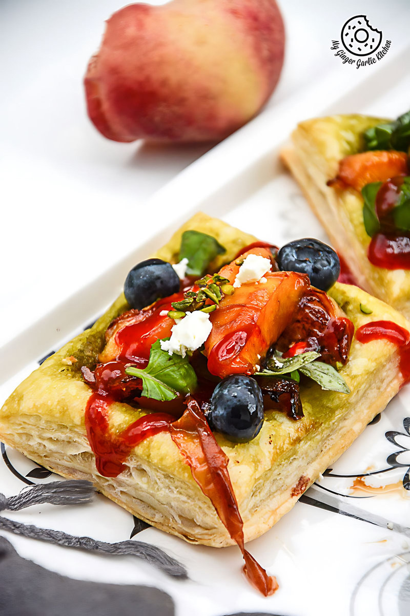 two pieces of peach pesto tart with blueberries and basils on a plate with a peach