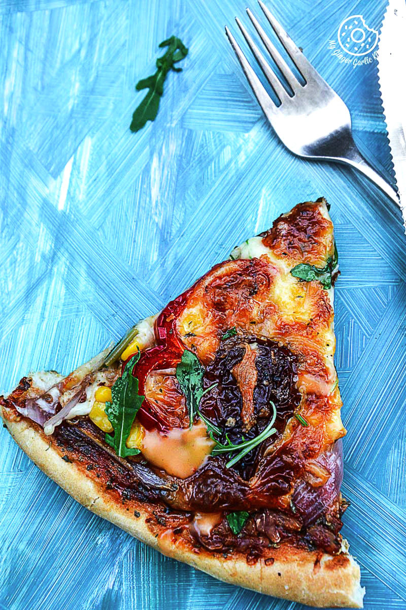 a slice of a pizza with pepper corn arugula pizza with sun dried tomatoes on a blue plate with a fork