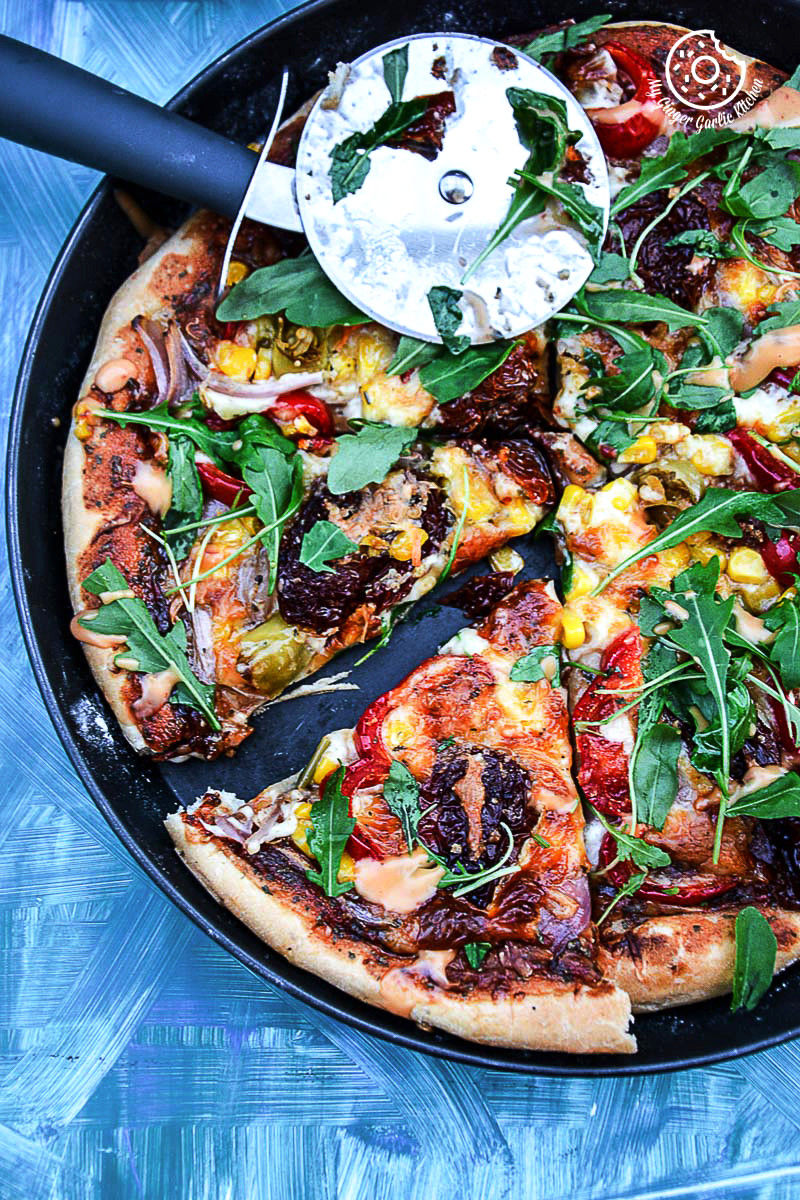 a pizza with pepper corn arugula pizza with sun dried tomatoes with a slice missing from it in a pan 