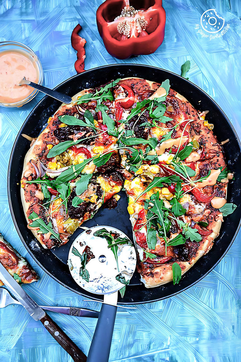 a pizza with pepper corn arugula pizza with sun dried tomatoes in a pan with a slice missing from it on a pan