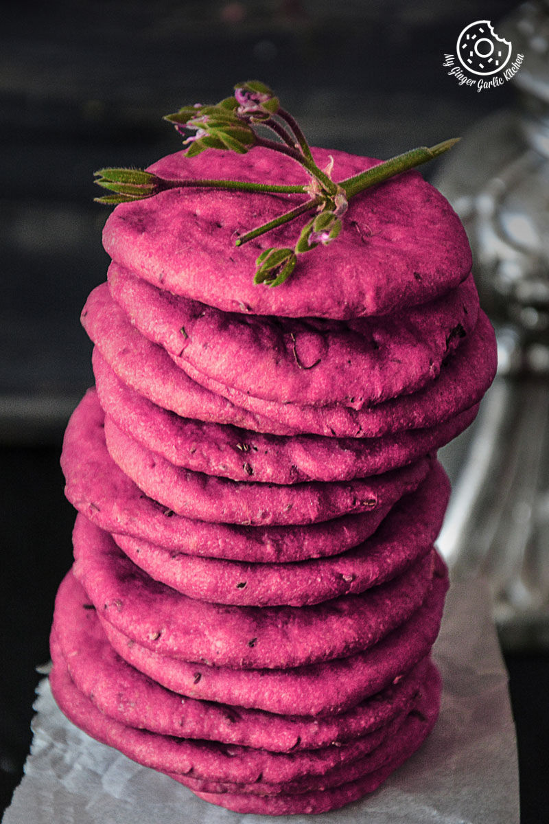 a stack of pink baked beet mathri with a sprig of green on top
