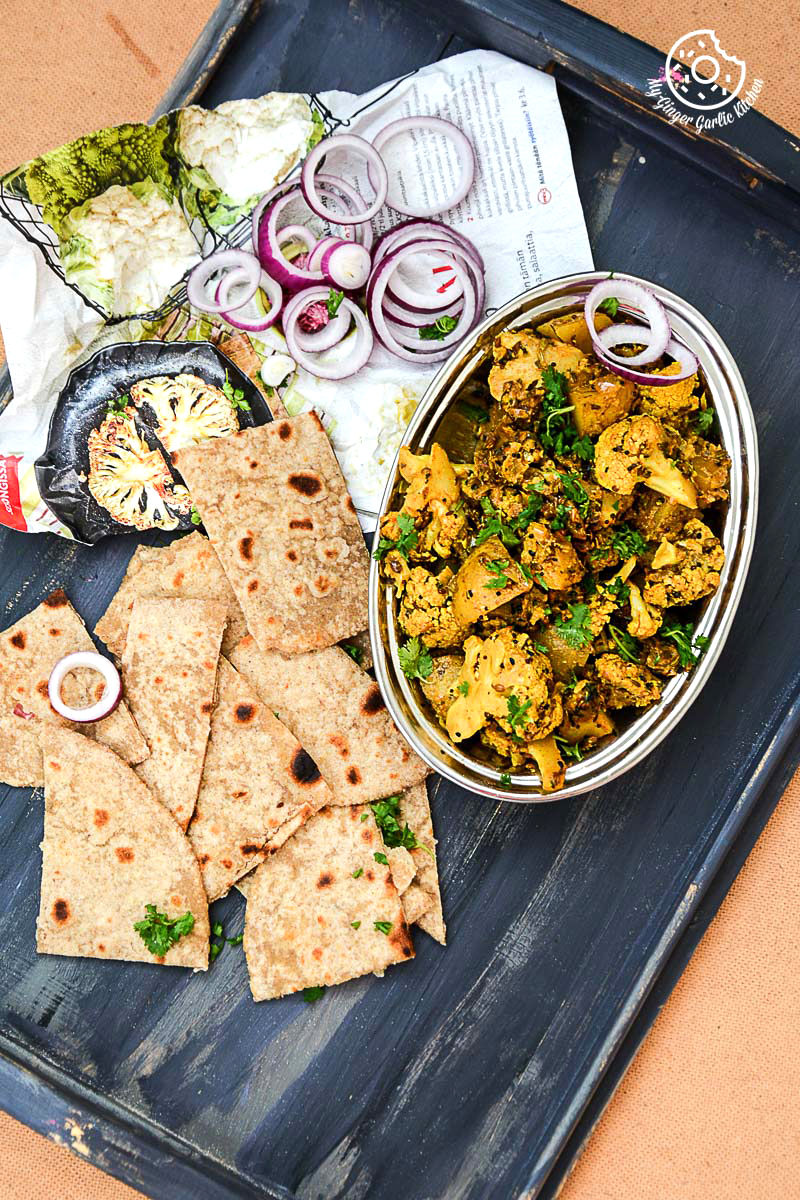 a tray with a bowl of achaari aloo gobi and parathas on it