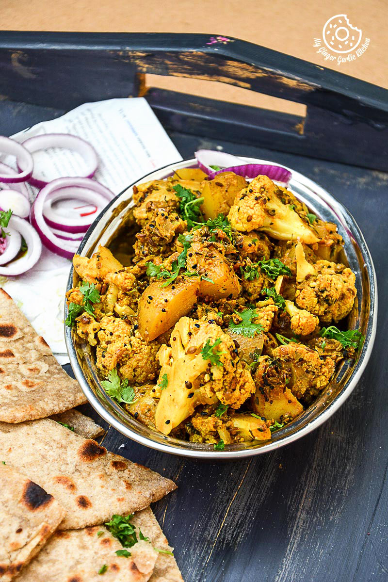 a bowl of achaari aloo gobi with some parathas bread and onions