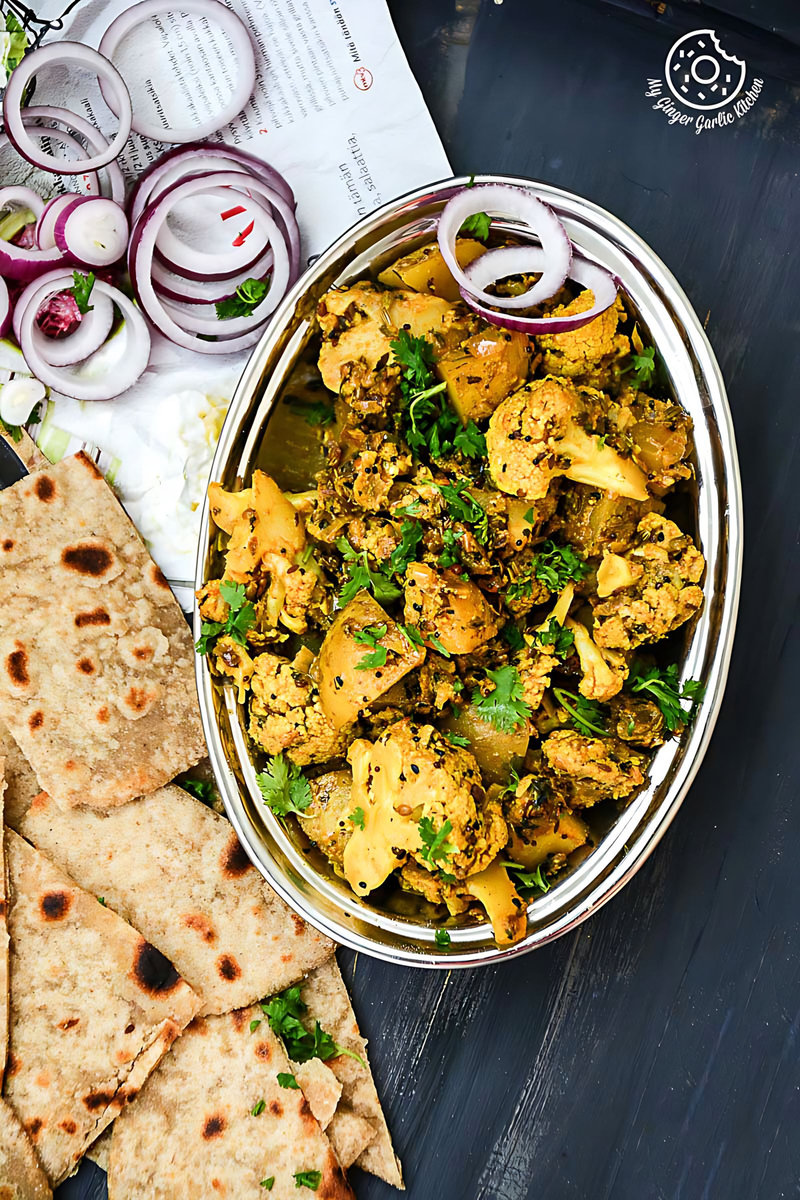a bowl of achaari aloo gobi with some parathas bread and onion