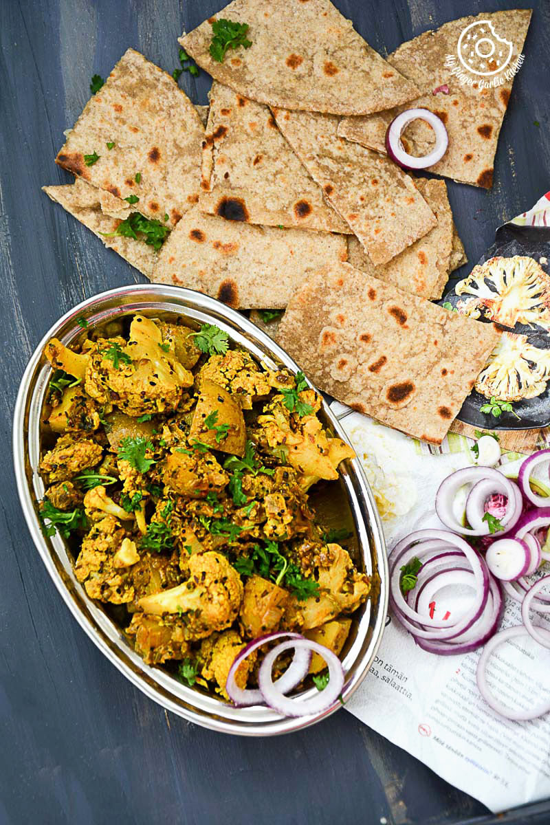 a bowl of achaari aloo gobi with parathas and onions