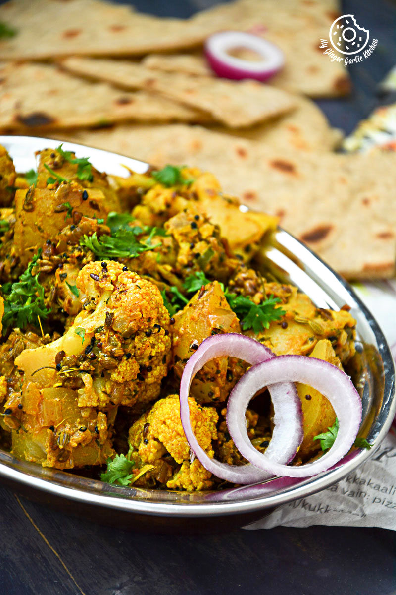 a plate of achaari aloo gobi with some plain parathas and onions