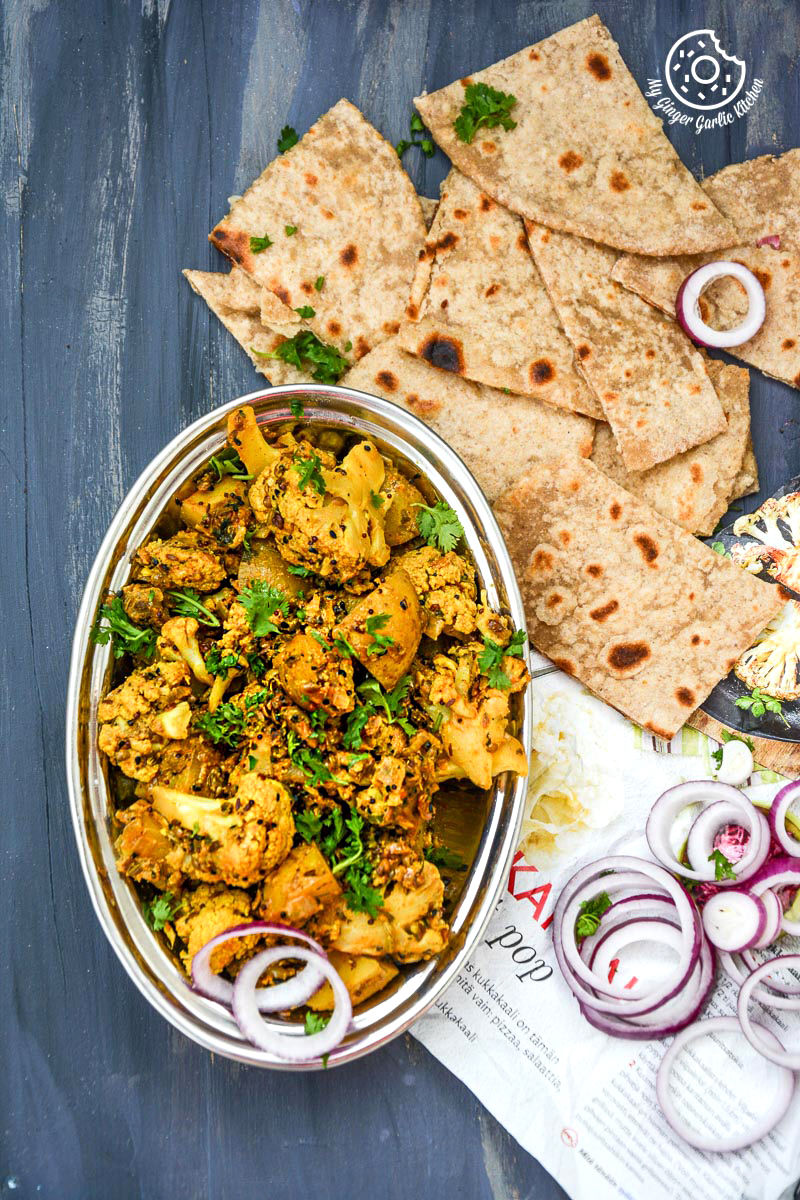 a bowl of achaari aloo gobi with a few paratha pieces and onion slices