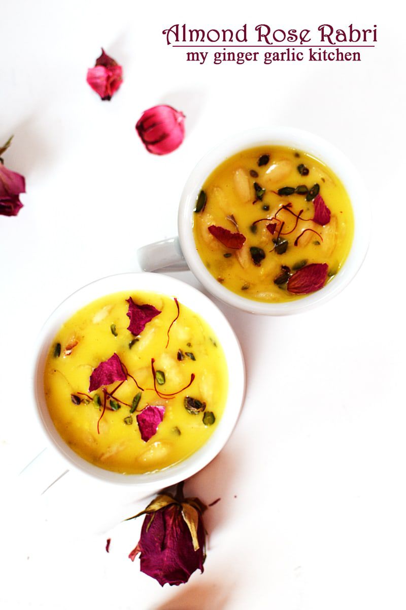 two bowls of almond rose rabri with flowers and petals on a white surface