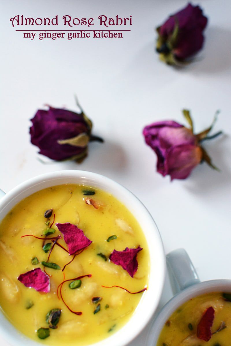 a bowl of almond rose rabri with some dried rose petals with a spoon and a rose on the side