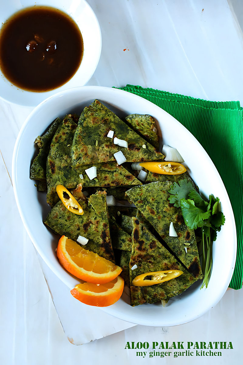 a plate of aloo palak paratha with orange slices and sauce