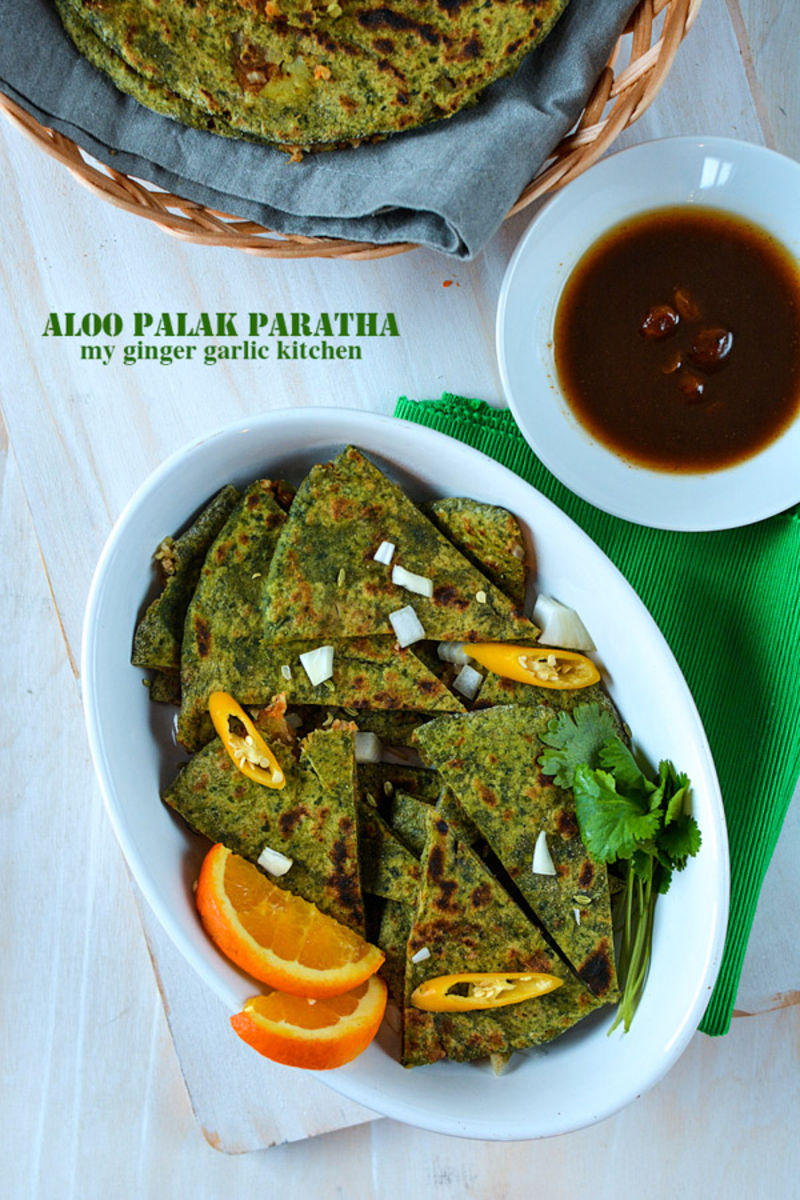a plate of aloo palak paratha with a bowl of sauce and a basket of parathas