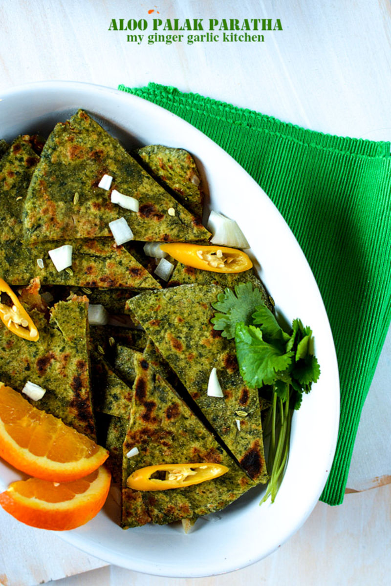 a plate of aloo palak paratha pieces with orange slices and a green napkin