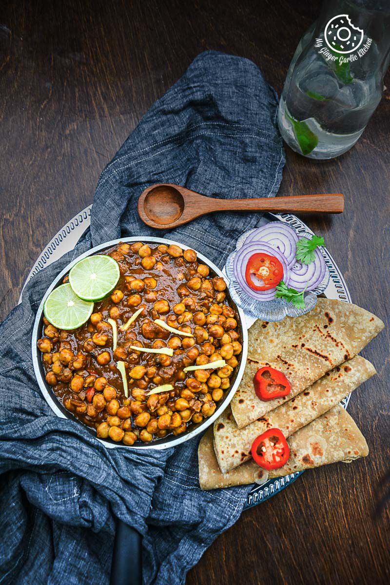 a bowl of amritsari chole topped with lime wedges, with some onion slices and parathas on a table