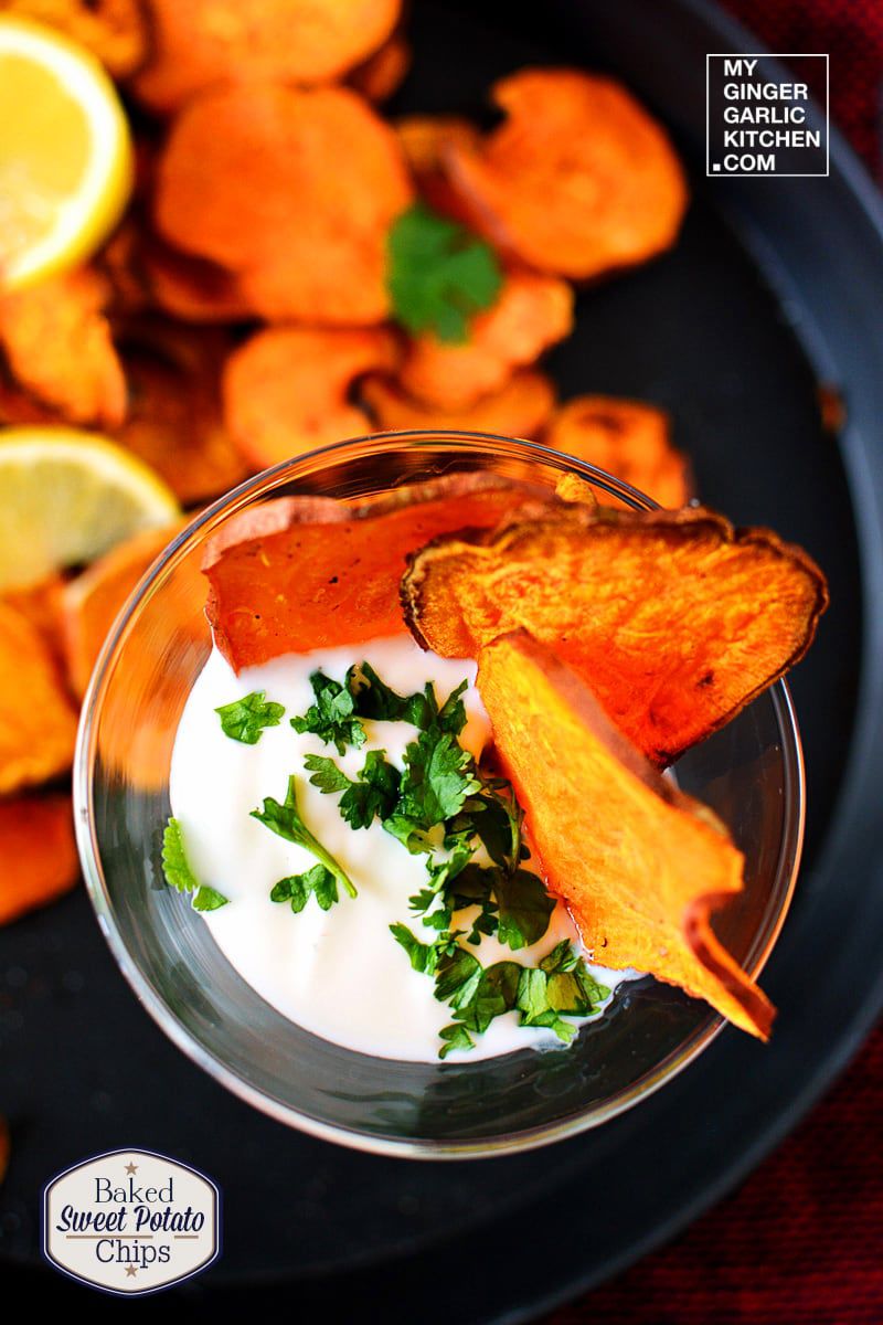 a plate of baked sweet potato chips with a glass of dipping sauce baked chips and green garnish