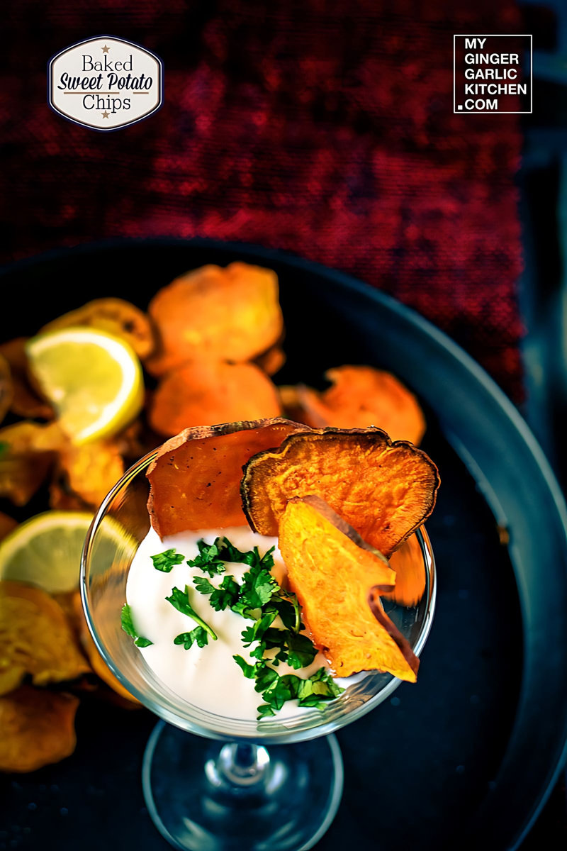 a small glass of dipping sauce on a plate with  baked sweet potato chips and lemon wedges