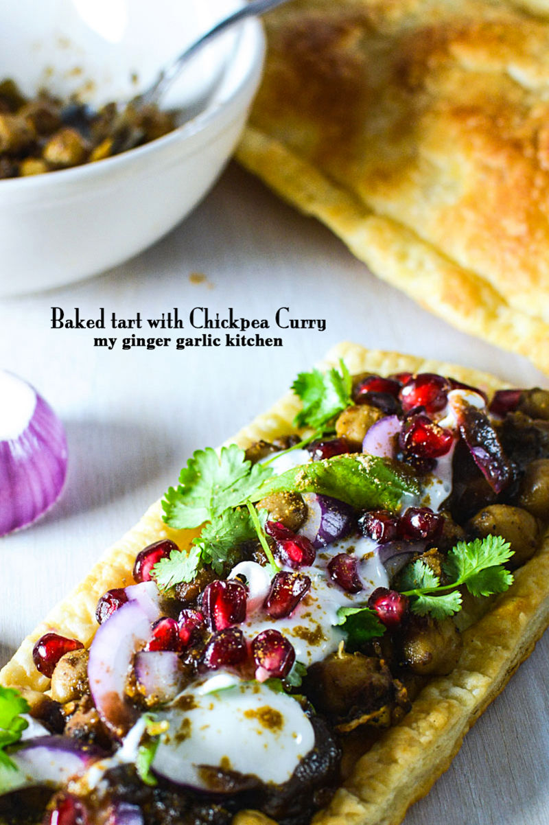 a baked tart with chickpeas curry and tamarind chutney with chickpeas, onions, and pomegranate on it