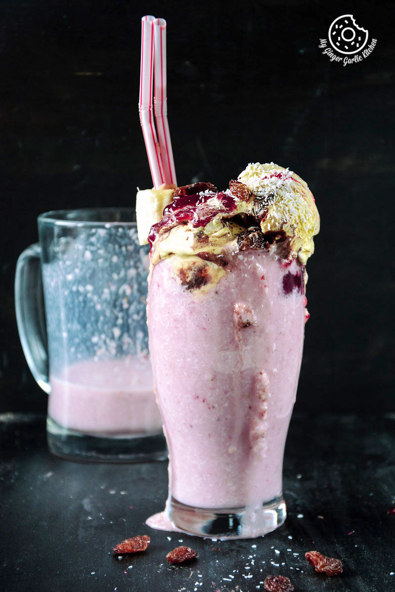 a glass of a banana raspberry coconut smoothie with tiramisu chocolate with a straw and a spoon