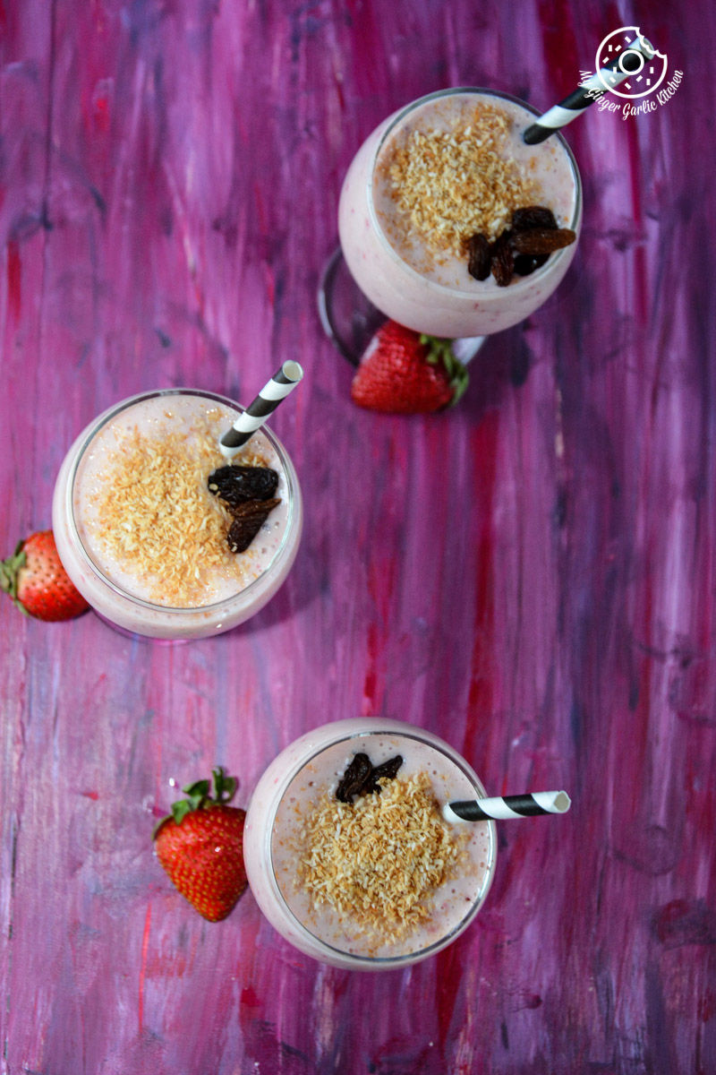 three glasses of banana strawberry coconut smoothies with strawberries and chocolate on a table