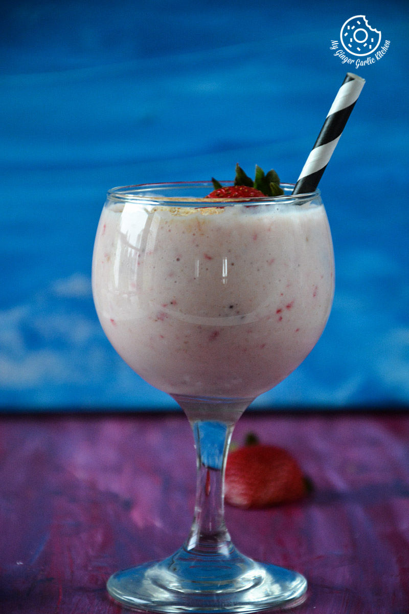 a glass of banana strawberry coconut smoothie with strawberries and a straw in it