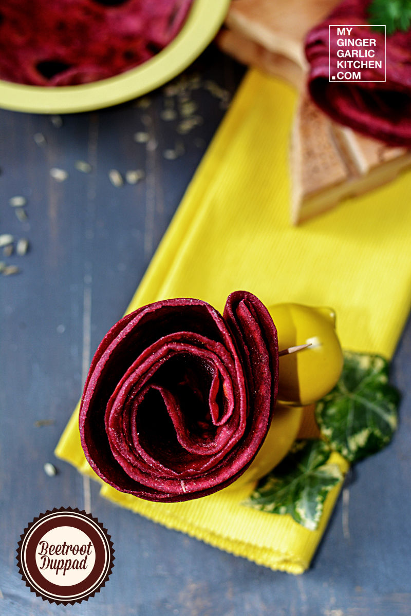 yellow napkin with a red colour beetroot duppad roti rolled in a flower shape on it sitting on a table