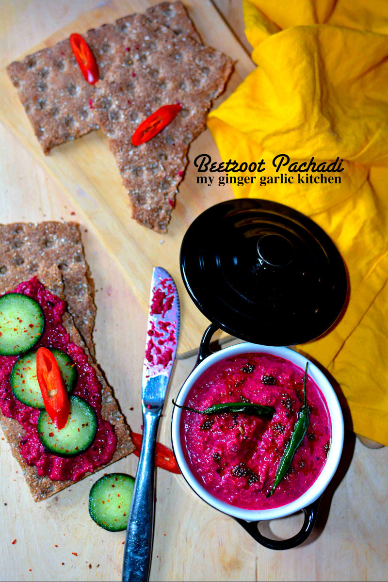 a bowl of kerala style beetroot pachadi with some cucumbers and crackers on a cutting board