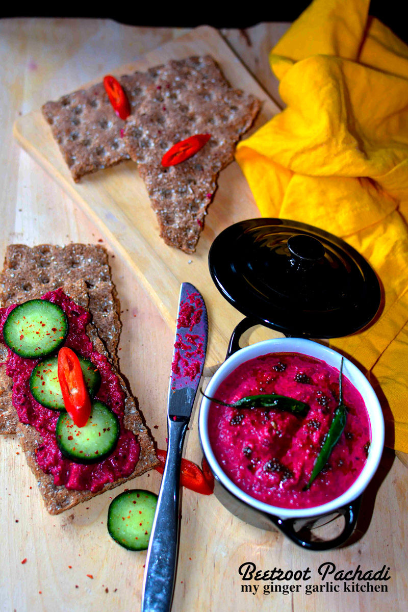 a bowl of kerala style beetroot pachadi with some cucumbers and crackers on a cutting board with a yellow napkin