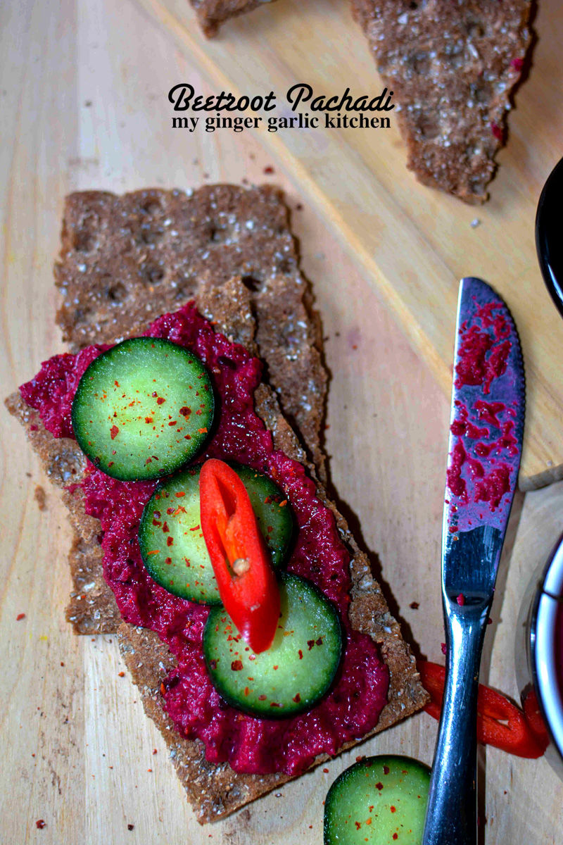 a piece of cracker with kerala style beetroot pachadi, cucumbers and a knife