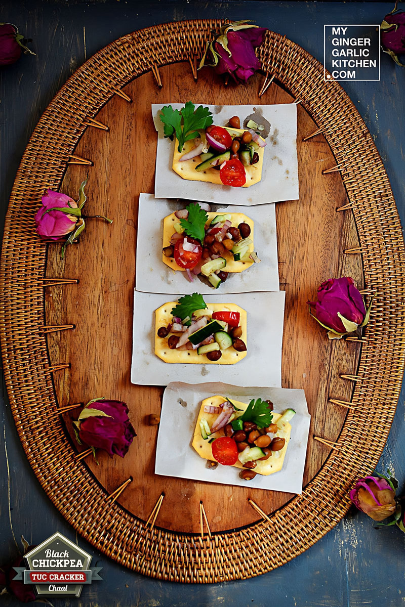 four small crackers with black chickpea tuc cracker chaat on a wooden tray with flowers